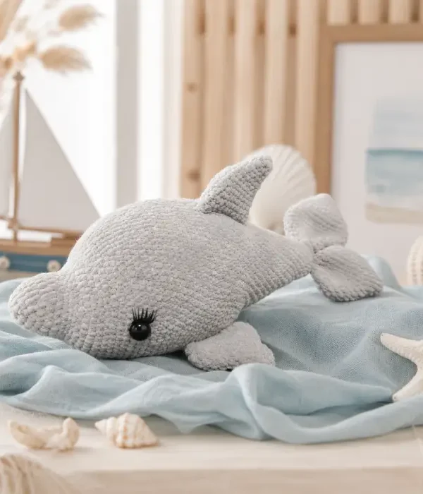 Doudou dauphin au crochet artisanal dans un univers marin doux Doudou dauphin au crochet artisanal gris posé sur un tissu bleu dans une décoration inspirée du bord de mer