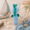 Doudou hippocampe au crochet artisanal – Vue arrière ambiance bord de mer Vue arrière d'un doudou hippocampe au crochet artisanal bleu et vert dans un décor marin avec voilier et coquillages