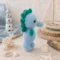Doudou hippocampe au crochet artisanal – Vue de profil dans un univers marin Doudou hippocampe au crochet artisanal bleu et vert photographié de profil dans une ambiance bord de mer